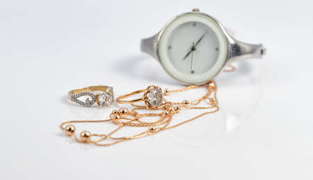 Gold diamond rings and a gold chain with beads lie against the background of a white women's watchの写真素材