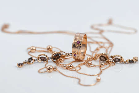 A gold ring with ruby inserts in the shape of stars, ruby earrings and a gold chain with beads are reflected on the white surfaceの写真素材