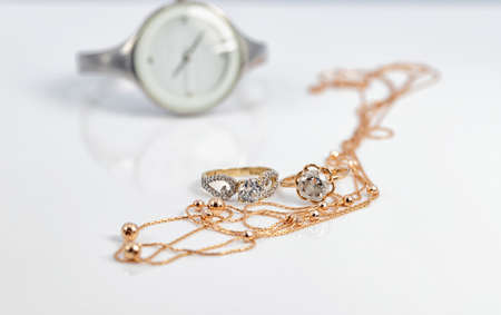 Gold diamond rings and a gold chain with beads lie against the background of a white women's watchの写真素材