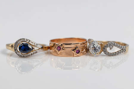 Three women's gold rings of different shapes and with different precious stones: diamonds, sapphire and rubyの写真素材