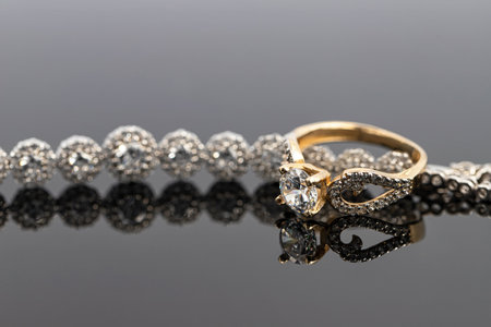 An elegant women's gold ring with a diamond is placed on a bracelet with precious stones. Dark backgroundの写真素材
