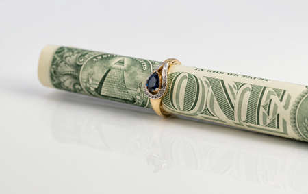 A gold sapphire ring is worn on a dollar bill rolled up into a tubeの写真素材