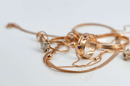 A gold ring with a bas relief in the shape of stars decorated with rubies and gold chains of various shapes and weaves on a white reflective surfaceの写真素材