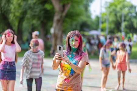 ESSENTUKI- JUNE 20: A girl with a painted face takes a selfie on her phone at the festival of colors. June 20, 2021 in Essentuki, Russia.のeditorial素材