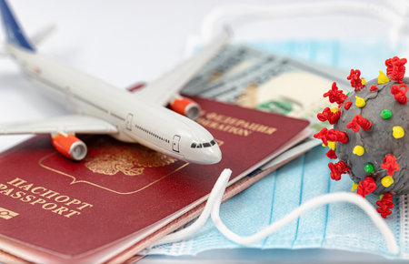 Protective medical masks, dollars, a passport, a model airplane and a 3D model of the virus lie nearbyの写真素材