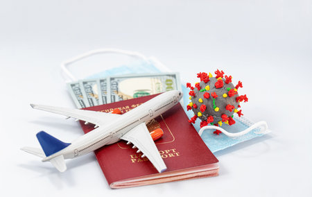 Protective medical masks, dollars, a passport, a model airplane and a 3D model of the virus lie nearbyの写真素材