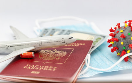 Protective medical masks, dollars, a passport, a model airplane and a 3D model of the virus lie nearbyの写真素材