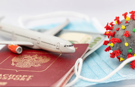 Protective medical masks, dollars, a passport, a model airplane and a 3D model of the virus lie nearbyの写真素材