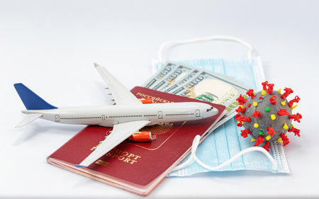 Protective medical masks, dollars, a passport, a model airplane and a 3D model of the virus lie nearbyの写真素材