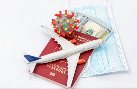 Protective medical masks, dollars, a passport, a model airplane and a 3D model of the virus lie nearbyの写真素材