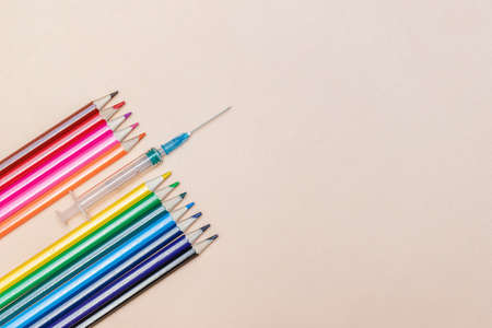 An empty syringe with a needle lies among the colored pencilsの写真素材