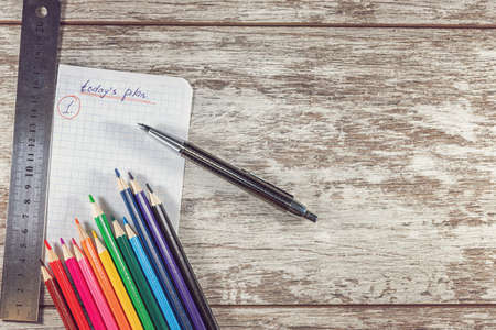 A piece of paper from a notebook with a plan for today, colored pencils, a pen and a metal ruler lie...