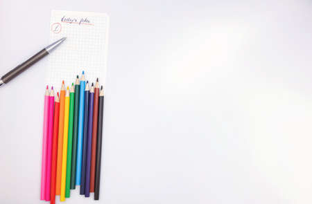 A piece of paper from a notebook with a plan for today, colored pencils, a pen and a metal ruler lie on a beige backgroundの写真素材