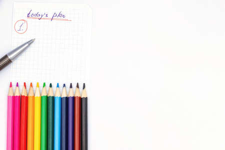 A piece of paper from a notebook with a plan for today, colored pencils, a pen and a metal ruler lie on a beige backgroundの写真素材