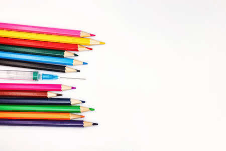 An empty syringe with a needle lies among the colored pencilsの写真素材