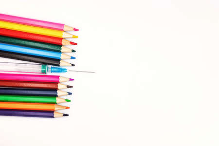 An empty syringe with a needle lies among the colored pencilsの写真素材