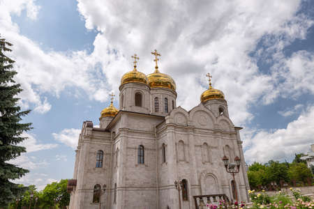 Large Orthodox church with white-stone facade and gilded domes against the background of cloudsの写真素材