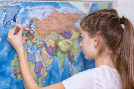 A girl holds a model of a passenger plane over a world map depicting an international flightの写真素材