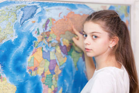 A school student studies geography on a large map of the world on the wall. She points her finger at the countries on the map.の写真素材