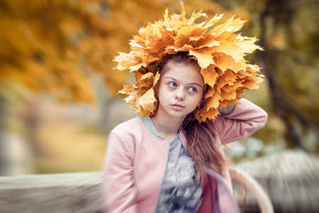 A girl in a city park tries on a wreath of yellow autumn leavesの写真素材