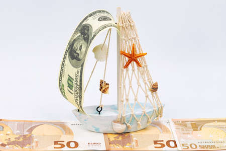 A ship with a sail of one hundred dollar bills sails along the fairway of European moneyの写真素材
