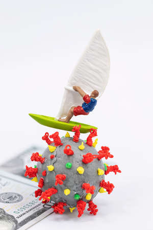 Toy windsurfer rides on hundred-dollar bills surrounded by 3D models of coronavirusの写真素材