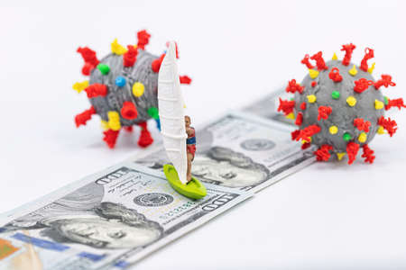 Toy windsurfer rides on hundred-dollar bills surrounded by 3D models of coronavirusの写真素材
