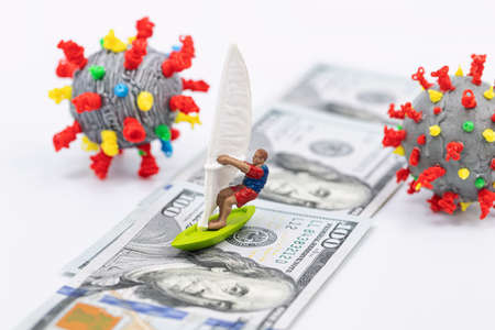 Toy windsurfer rides on hundred-dollar bills surrounded by 3D models of coronavirusの写真素材
