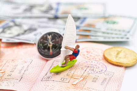 Toy windsurfer rides on waves of money and passport pagesの写真素材