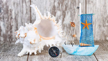 Toy boats and a large white seashell lie on a wooden backgroundの写真素材