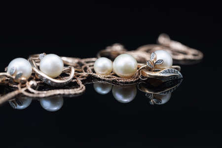 Gold earrings and rings with white pearls lie on a black mirror surfaceの写真素材