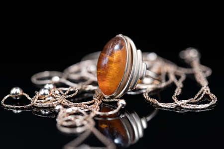 Elegant gold chain and gold ring with amber lie on a black reflective surfaceの写真素材