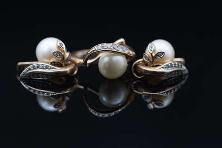 Gold earrings and rings with white pearls lie on a black mirror surfaceの写真素材