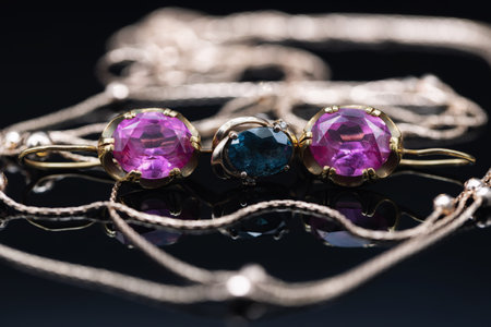 Gold earrings with large rubies and an elegant gold chain lie on a black mirror surfaceの写真素材