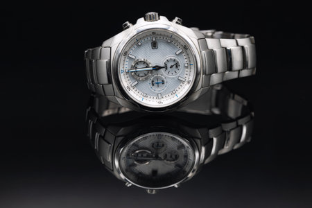 Stylish expensive men's wristwatch with a chronometer in a titanium case lies on a black reflective surfaceの写真素材