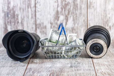 Two photo lenses and a toy basket with money lie on a wooden backgroundの写真素材