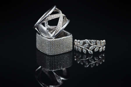 Silver women's rings of different shapes and sizes on a black mirror surfaceの写真素材