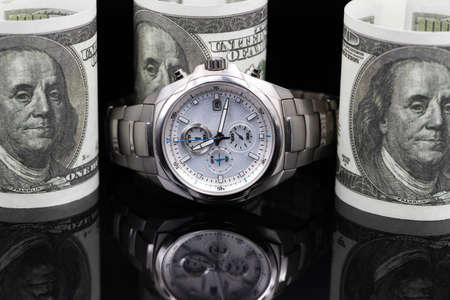 Expensive men's watch with a chronometer in a titanium case lies surrounded by dollar billsの写真素材