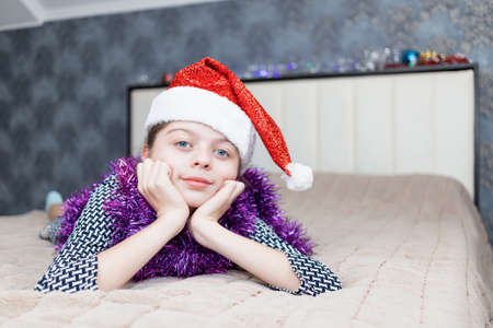 Charming girl lies on a large bed with a Santa Claus cap on her headの写真素材