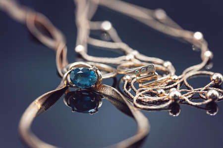 Gold rings with different precious stones lie surrounded by beautiful gold chainsの写真素材