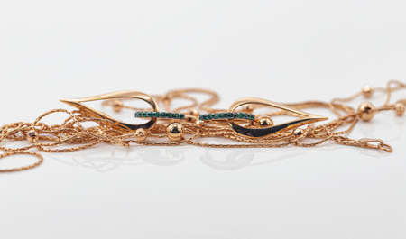Elegant gold earrings in the shape of a drop with emeralds lie surrounded by a thin gold necklaceの写真素材