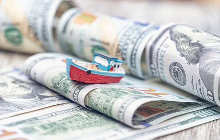A small toy boat overcomes waves of dollar billsの写真素材