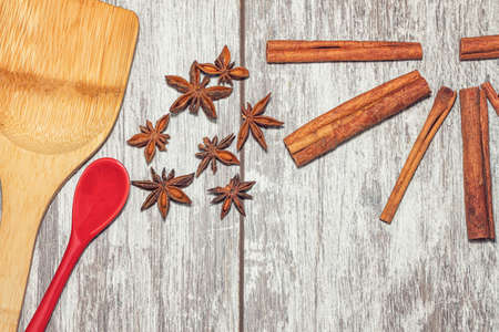 Cinnamon, anise, star anise and a porcelain tea spoon lie on a wooden surface.の写真素材