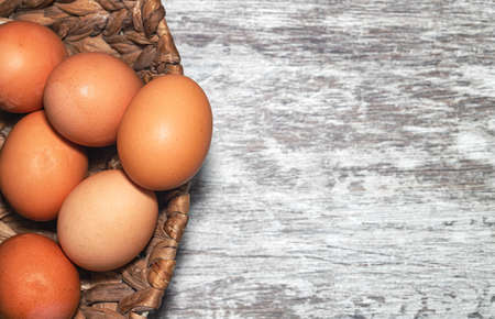 Unpainted chicken eggs lie in a handmade wicker basket on a wooden background