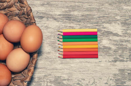 Easter background on a wooden surface with unpainted eggs and colorful pencilsの写真素材