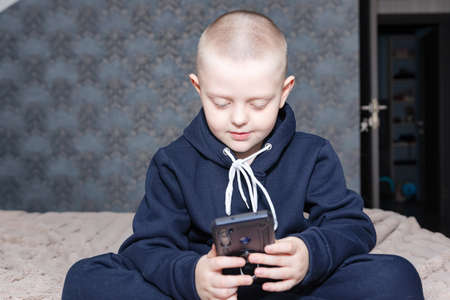 A preschool boy in a blue hoodie looks at a smartphoneの写真素材