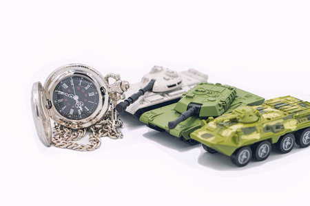 Three toy tanks and a pocket watch on a white backgroundの写真素材