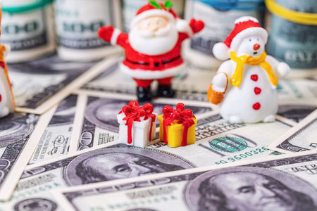 Toy figures of Santa Claus and snowman stand on scattered dollar billsの写真素材