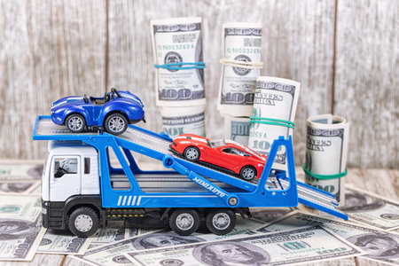 Toy trailer transports passenger toy cars against the background of scattered dollar billsの写真素材