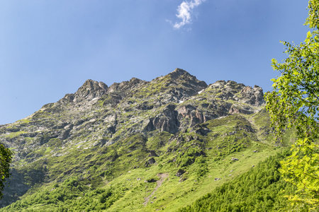Mountain landscape with green slopes, cliffs, glaciers and white fluffy clouds in the skyの写真素材